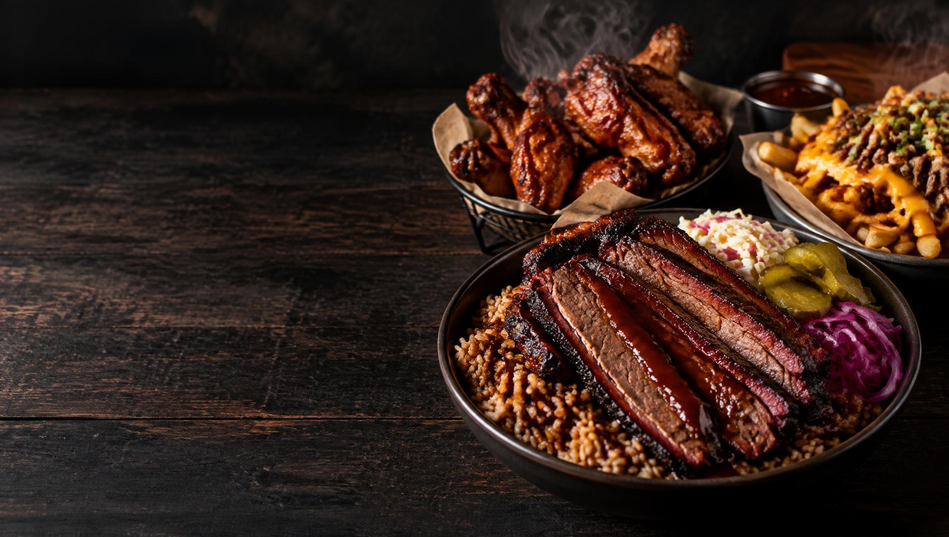 Smoked brisket bowl, wings and loaded fries on a dark table